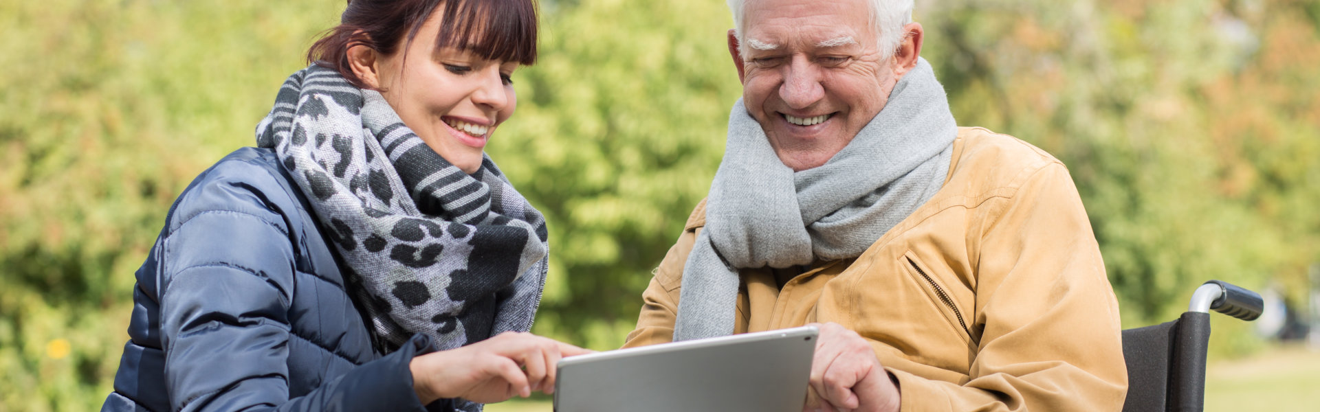 Smiling disabled senior and caregiver with a tablet